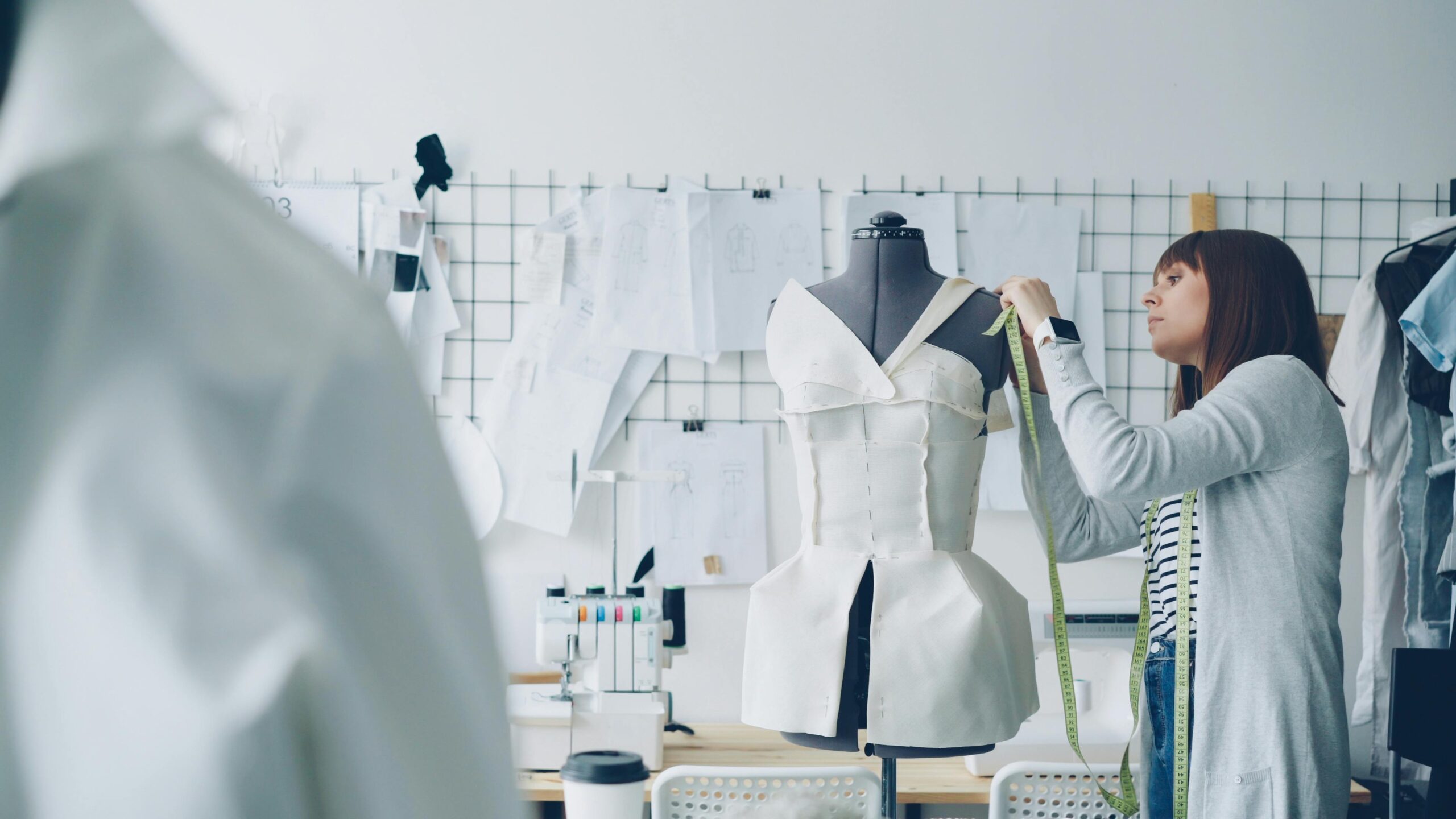 Female designer measuring white dress on mannequin in studio.